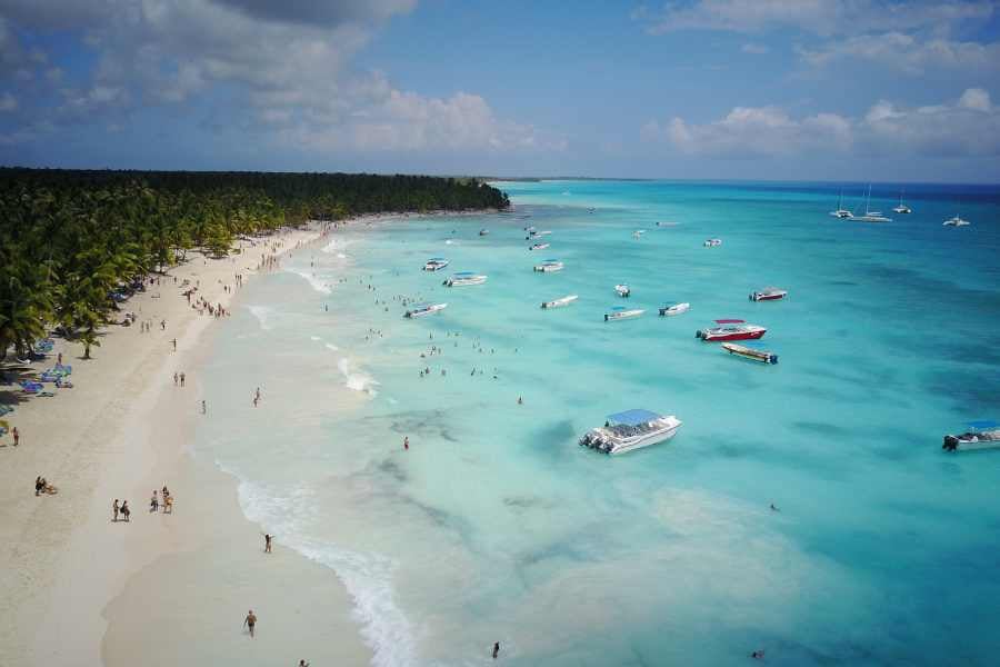 Boats dot the turquoise waters of a white sandy beach, with palm trees stretching into the distance.