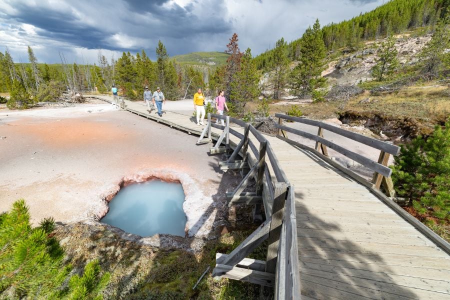 Tourists exploring a boardwalk by bright blue bubbling thermal pools.