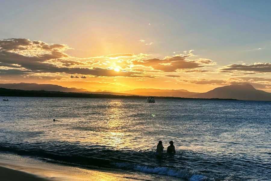 A serene sunset over the ocean with two people wading in the water.