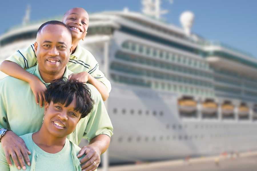 A smiling family stands together in front of a large cruise ship, enjoying their vacation.