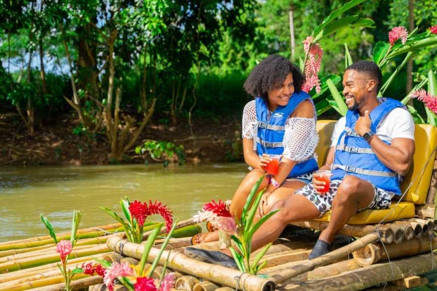 A cheerful couple relaxes on a decorated bamboo raft, sipping drinks and sharing smiles as they drift down the river.