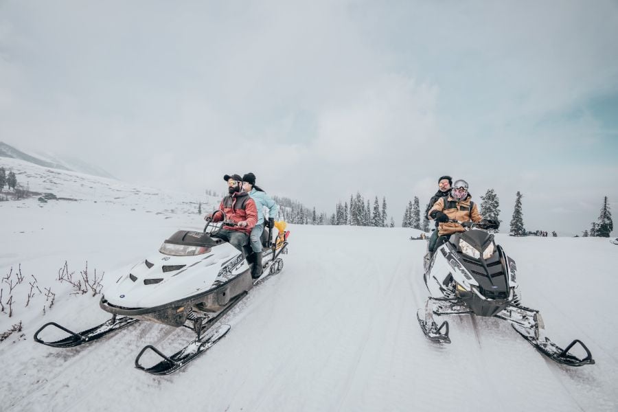 Friends snowmobiling together across wide-open fields in Vail.
