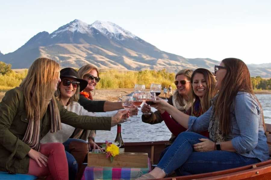 A group of friends toasts with wine, enjoying a scenic boat ride near the mountains.