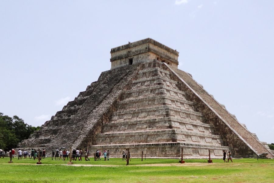 Tourists explore the grand pyramid of Chichen Itza under the warm Yucatán sun.