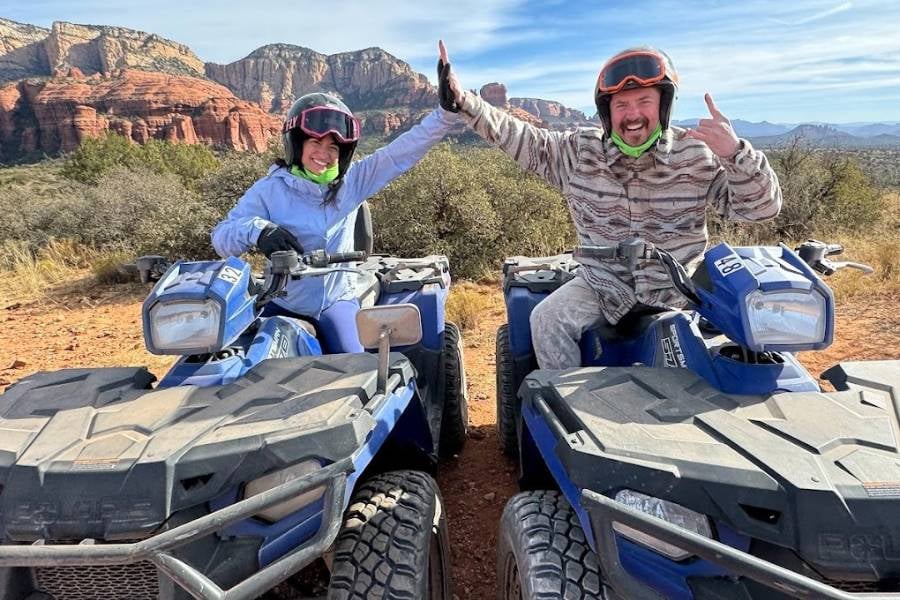 Two people wearing helmets are smiling and high-fiving while sitting on ATVs.