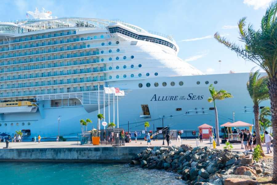 A large cruise ship, "Allure of the Seas," docked with passengers walking along the pier.