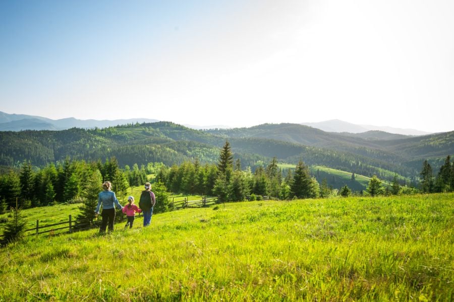 A family hikes through bright green hills, surrounded by endless forested mountains.