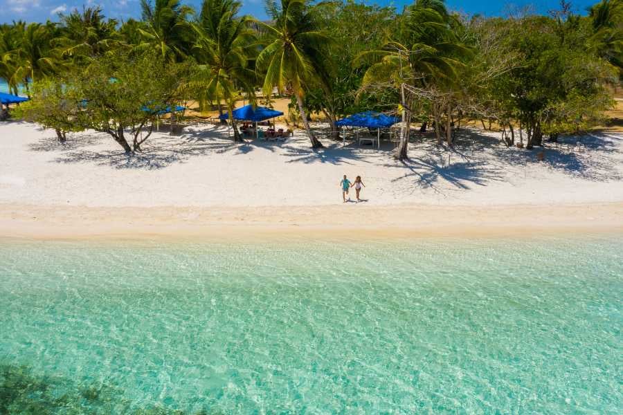 Two people walking along a pristine beach with blue umbrellas in the background, enjoying the serene surroundings.