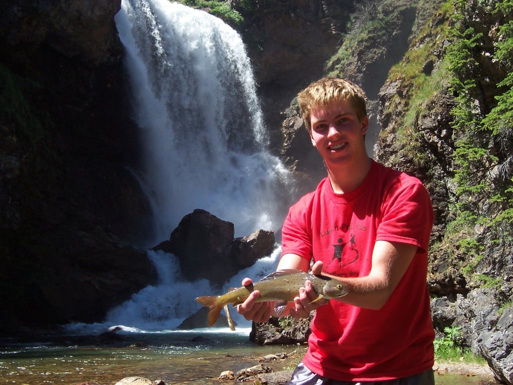 young man holding grayling in front of waterfall