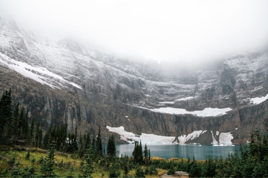 A foggy mountain lake sits beneath snowy cliffs.