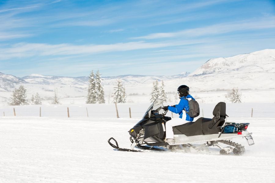 Rider speeds across snowy plains with Vail mountains in view.