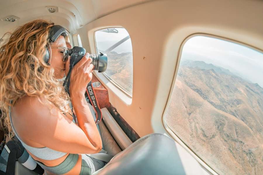  A woman takes photos from a small airplane, capturing the mountains through the window.