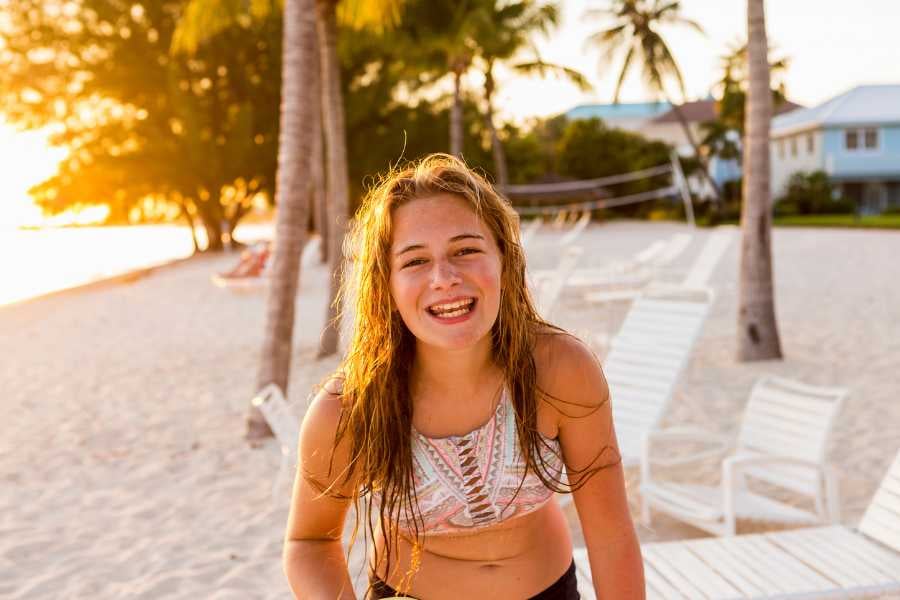 A smiling girl with wet hair enjoying the golden sunset, surrounded by palm trees and sandy beaches.