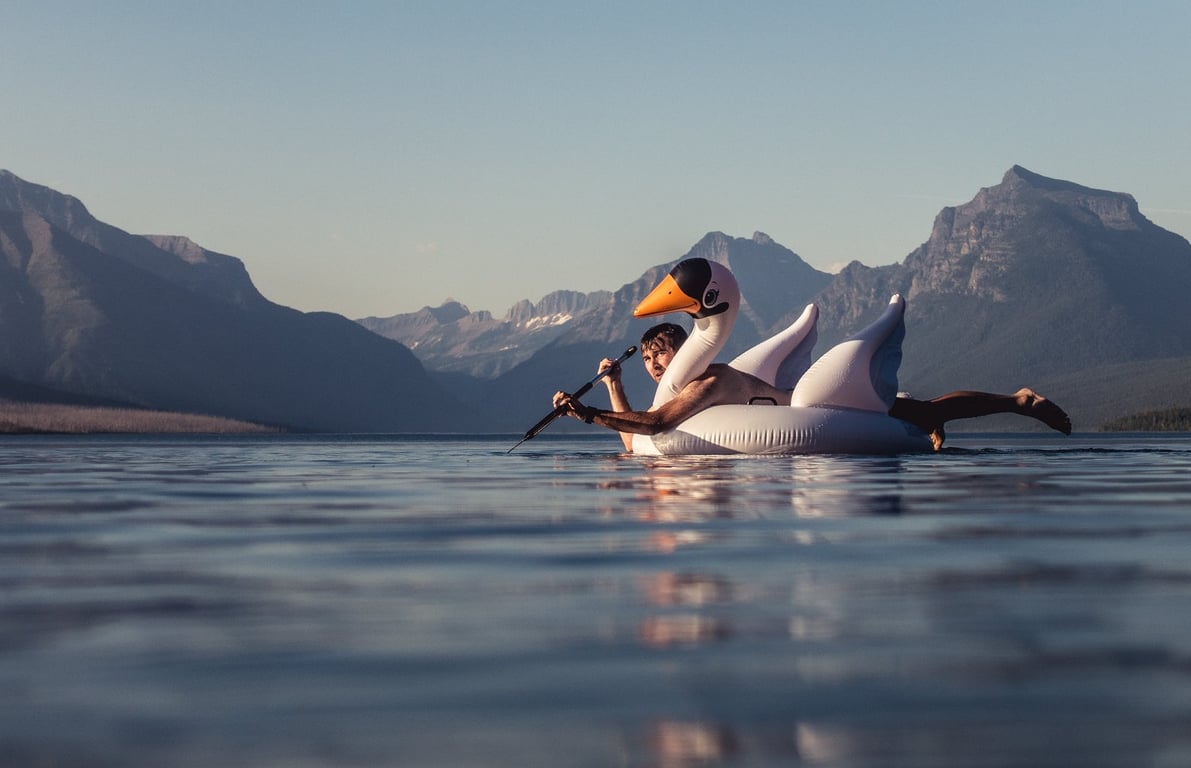 man swims on inflatable swan on lake mcdonald