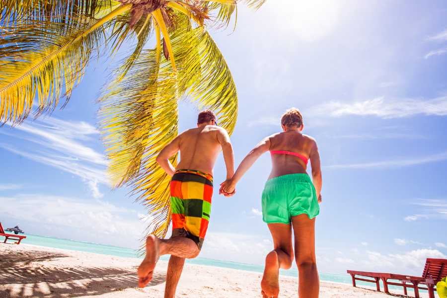 A couple joyfully runs toward the turquoise sea, surrounded by palm trees and endless blue skies.