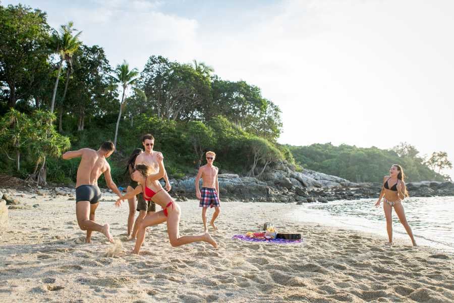 Friends laughing and playing on a secluded beach, surrounded by lush greenery and sparkling waves.