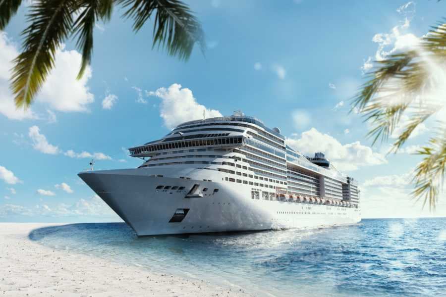 A cruise ship docked near a tropical beach, surrounded by palm trees and clear blue waters.