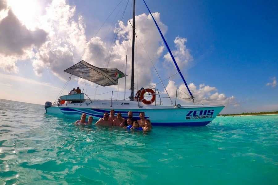 A group enjoys the crystal-clear ocean while a sleek catamaran floats nearby under a sunny sky.