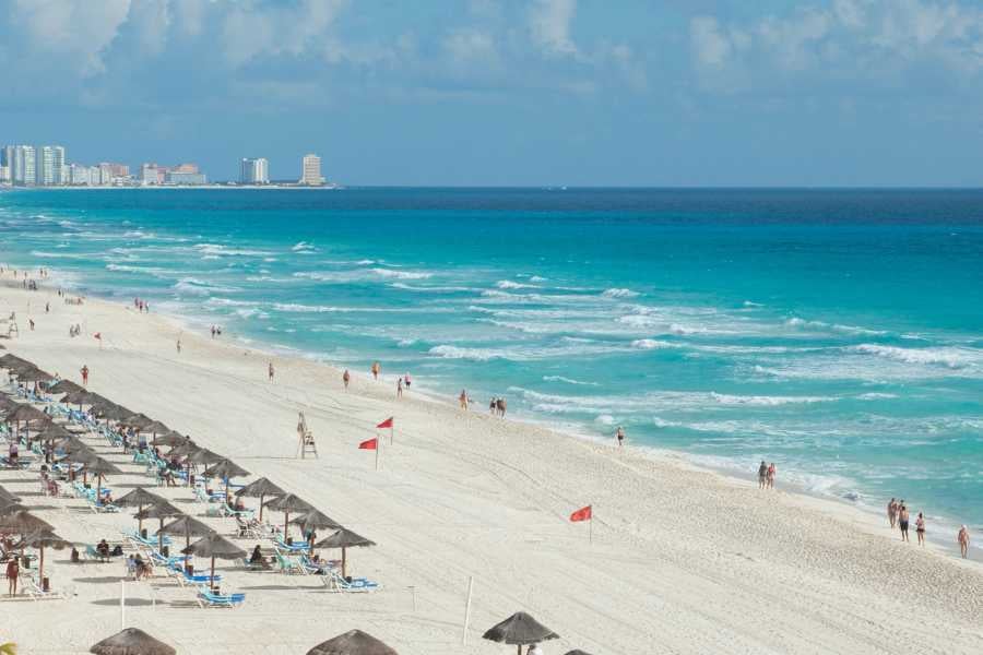 A white sandy beach lined with umbrellas and the vibrant blue Caribbean waters of Cancun.