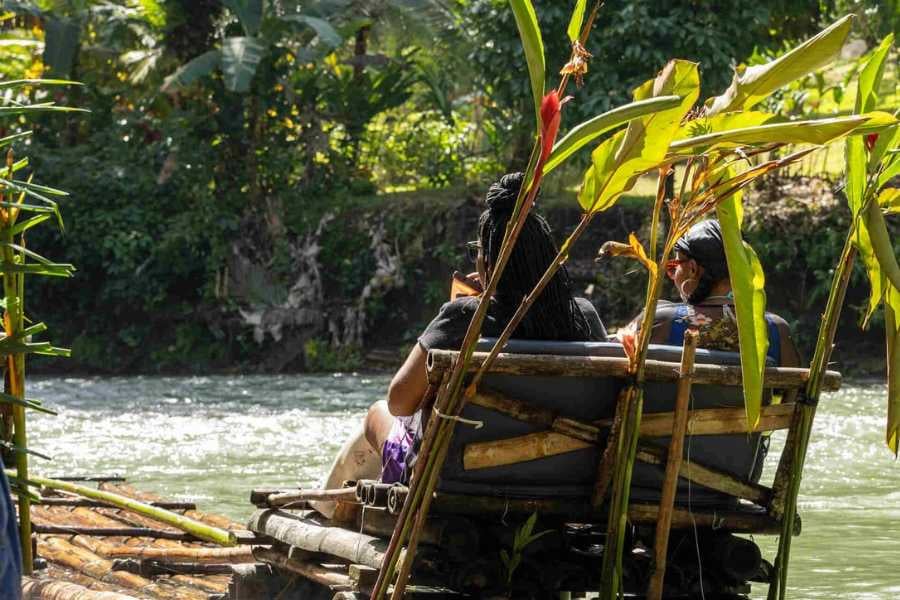 Two women enjoy a serene bamboo raft ride along a river, surrounded by lush greenery and a tranquil atmosphere.