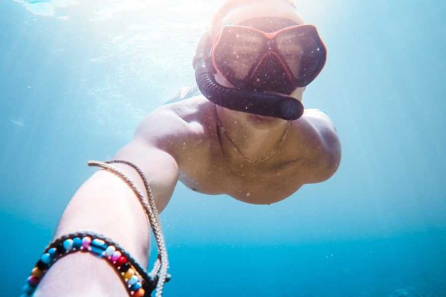 A snorkeler takes an underwater selfie, capturing the vibrant blue sea and shimmering sunlight above.