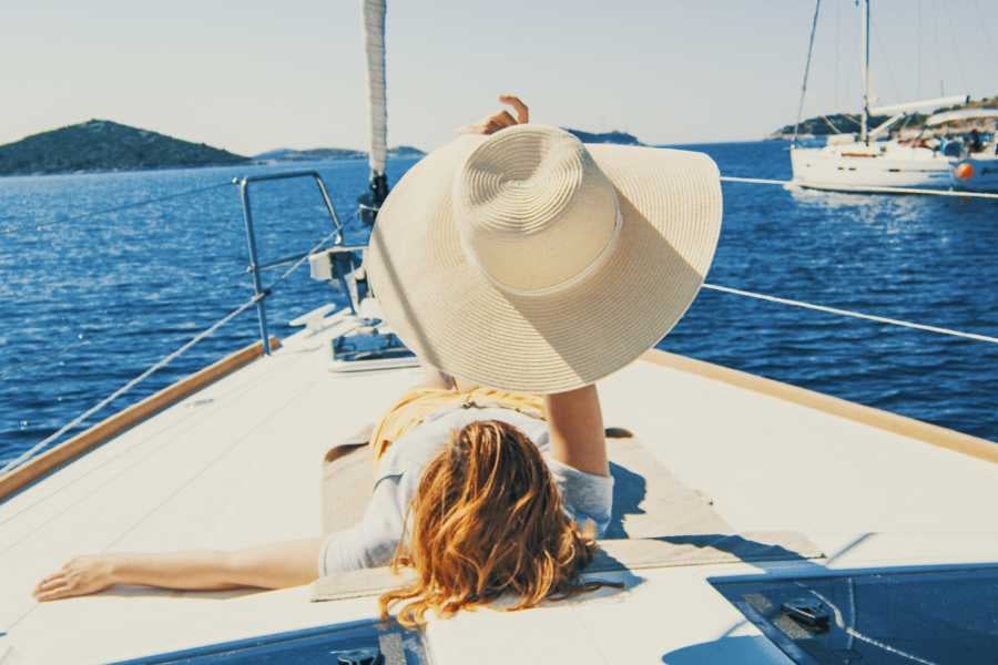 A woman reclines on a yacht deck, her wide sun hat shading her face as she basks in the sea breeze.