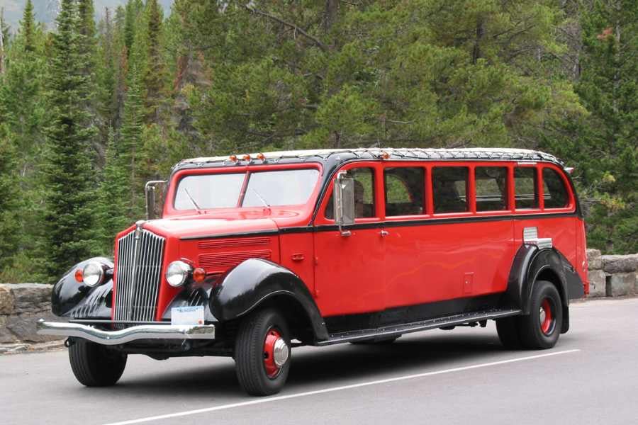 A classic red tour bus parked amidst a picturesque natural setting.
