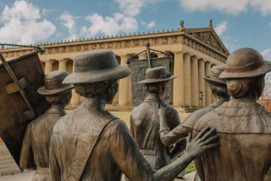 Bronze statues of women honor the suffrage movement outside a grand stone building.