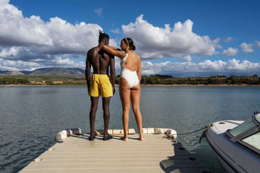 A couple stands on a dock, gazing at the tranquil waters with a boat nearby.