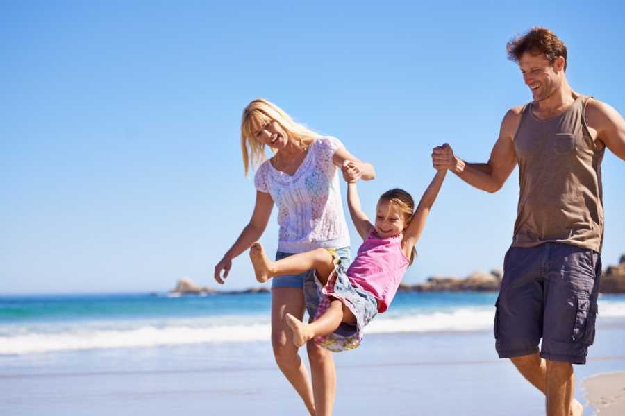  A happy family enjoys a sunny day, laughing and swinging their child on a beautiful sandy beach.