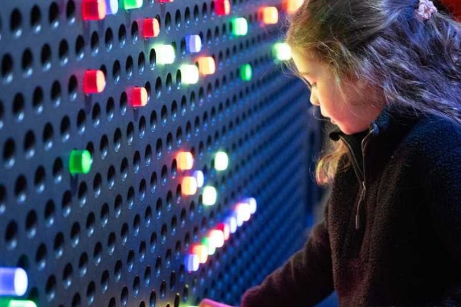A girl lights up a giant pegboard with colorful glowing pieces.