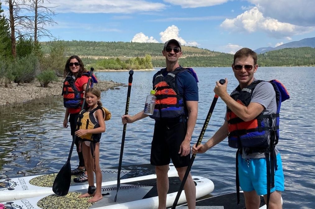 A family goes stand-up paddleboarding on a calm Breckenridge lake.