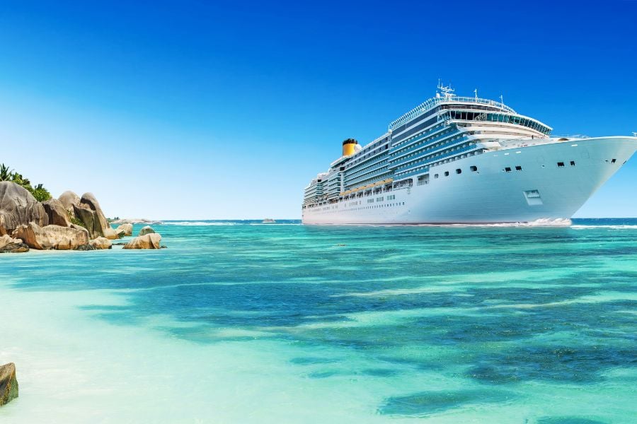 A bright white cruise ship sailing across clear turquoise water.
