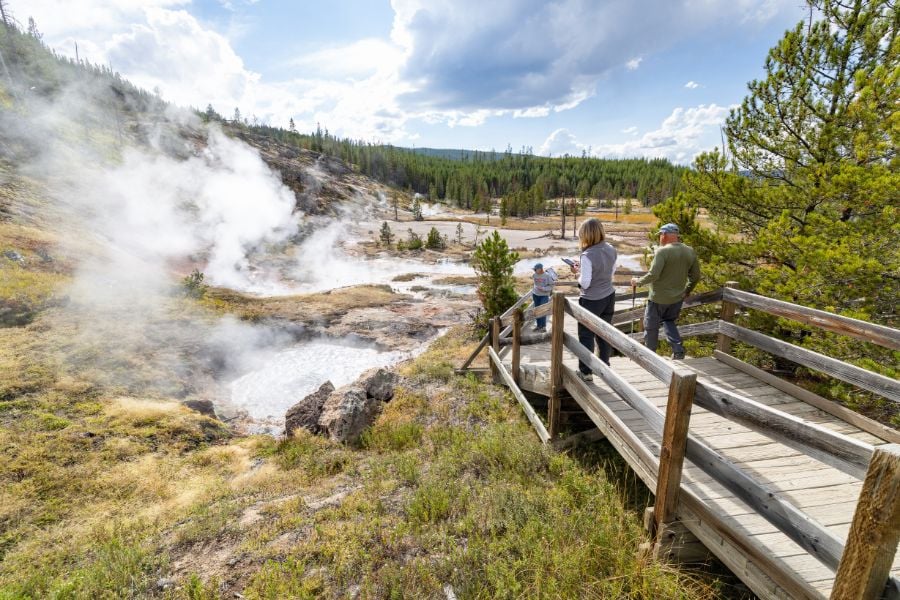 Visitors gazing at steaming geysers and pools in Yellowstone’s geothermal area.