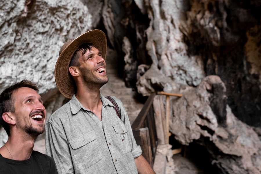 Two visitors smile in delight as they explore a rugged cave filled with fascinating formations and natural beauty.