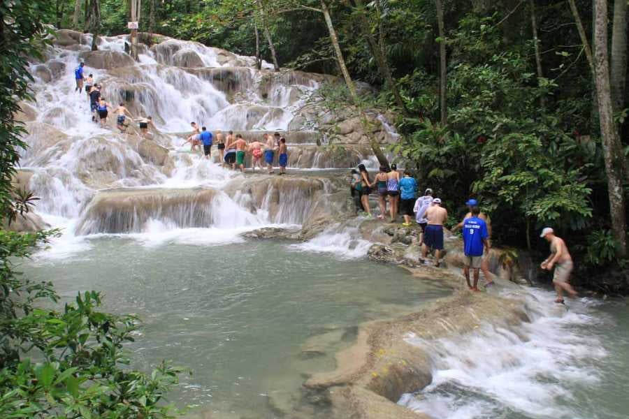 Visitors climb limestone steps as water cascades down a scenic waterfall.