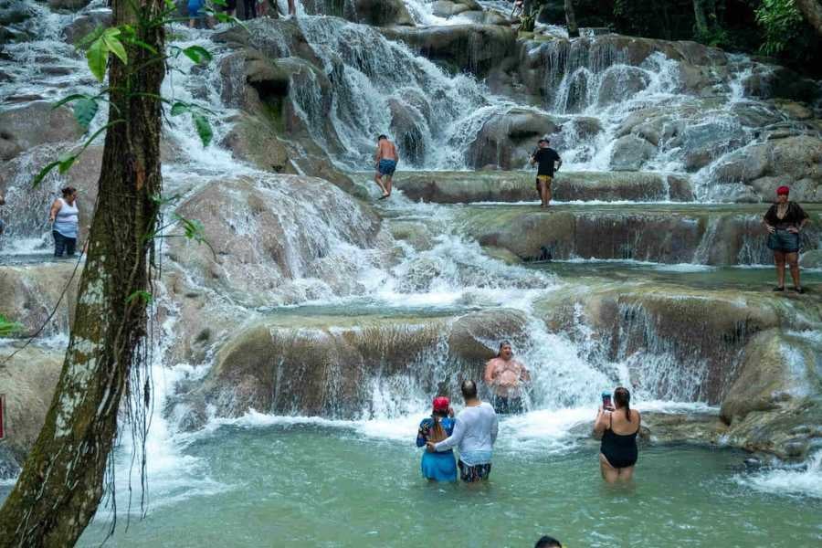 Visitors enjoying a lively waterfall, stepping through cool flowing water and taking in the tropical beauty.