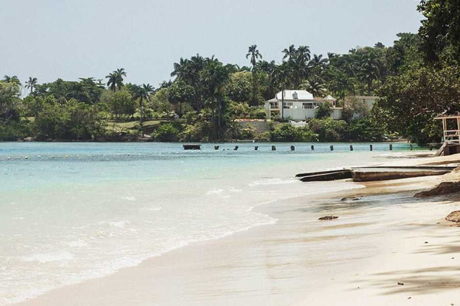 A peaceful beach with soft sand and calm waters, framed by tropical greenery and seaside cottages.