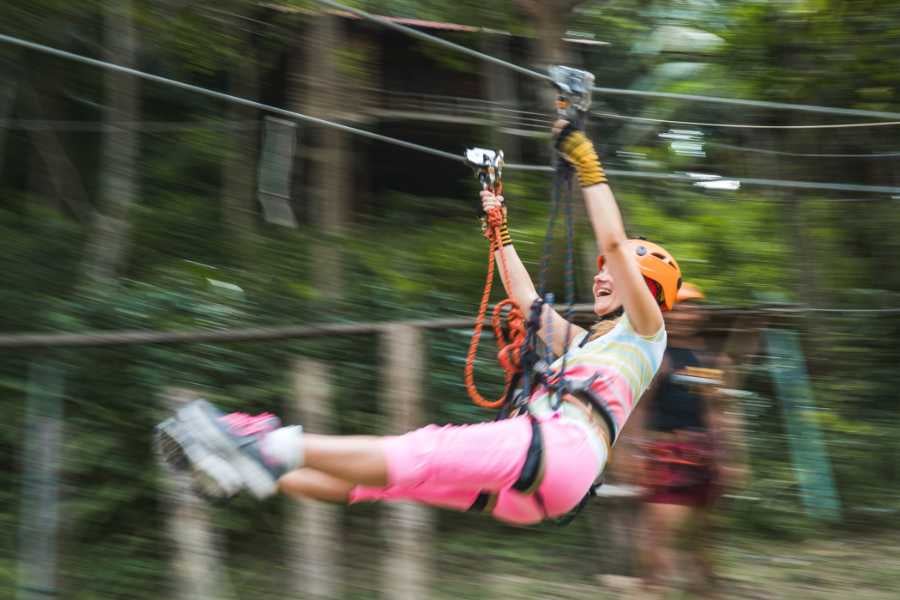 A woman thrills in mid-air while ziplining through a green forest, showing off her adventurous spirit.