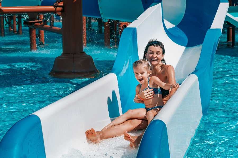 A mother and child enjoy a thrilling water slide adventure, splashing into a sparkling pool together.