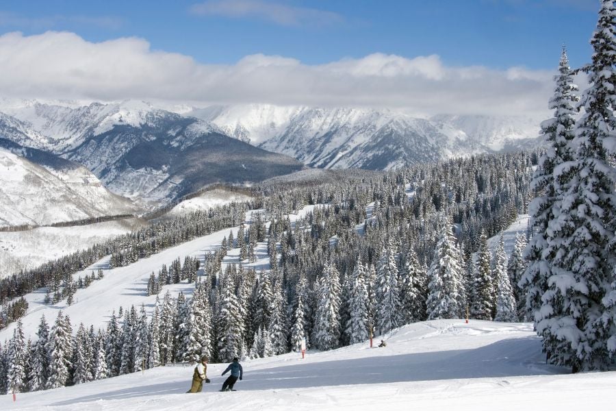 Skiers enjoy wide snowy slopes with mountain views stretching across the horizon.