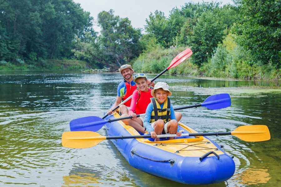 miling family paddles down a calm river in a bright blue kayak.