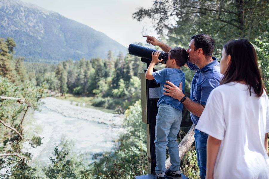 A family enjoys mountain views while using a telescope to spot wildlife.