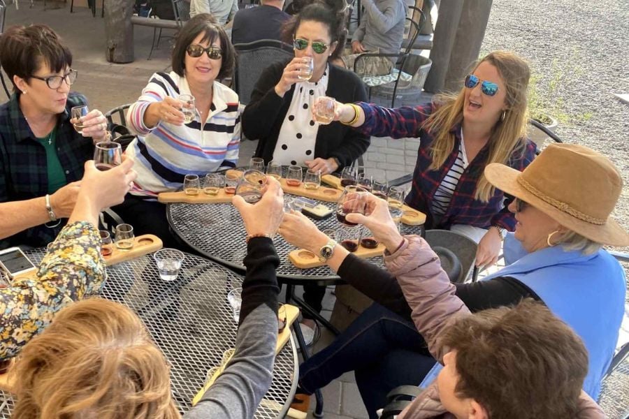 A big group of friends cheers with colorful drinks at a patio table.
