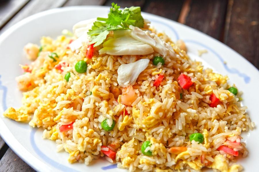 A bright plate of fried rice with vegetables and crab meat topping.
