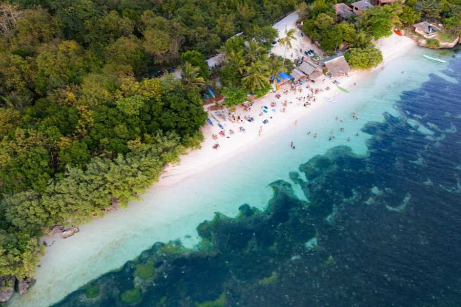 An aerial view of a peaceful beach with crystal-clear water and people relaxing under the sun.