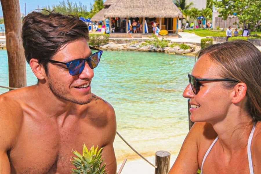 A couple shares smiles over tropical drinks by the clear, calm water at a beachside cafe.