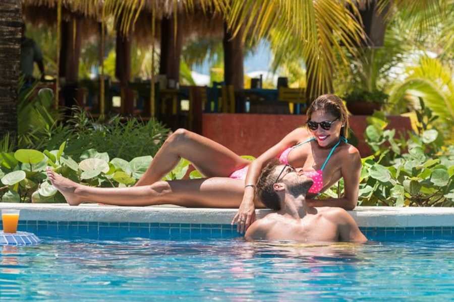 A couple relaxes in a tropical resort pool, surrounded by palm trees, with a cool drink within reach.