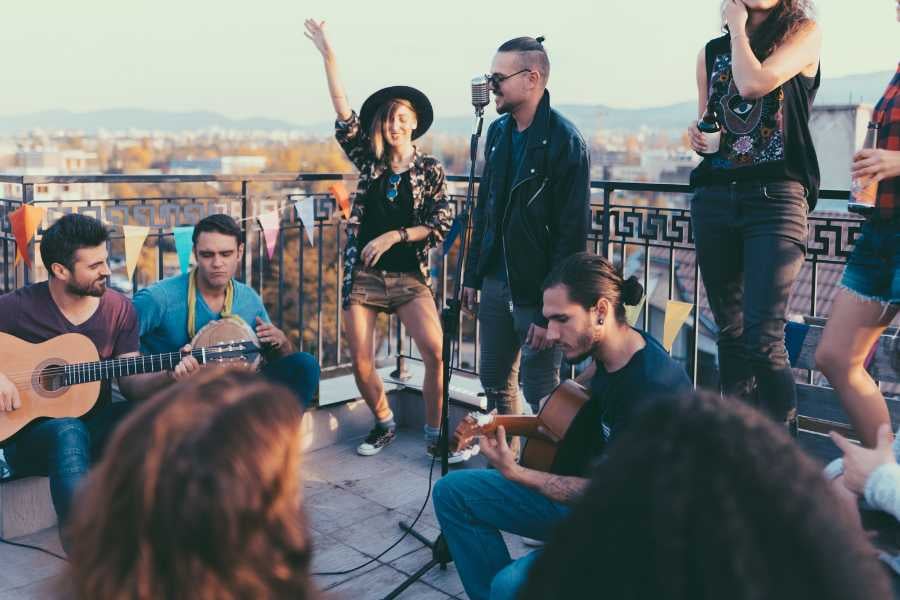 A lively rooftop gathering with friends enjoying live music, singing, and the warm glow of the sunset.