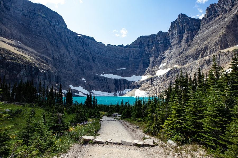 A mountain trail leads to a stunning turquoise lake surrounded by rocky peaks.
